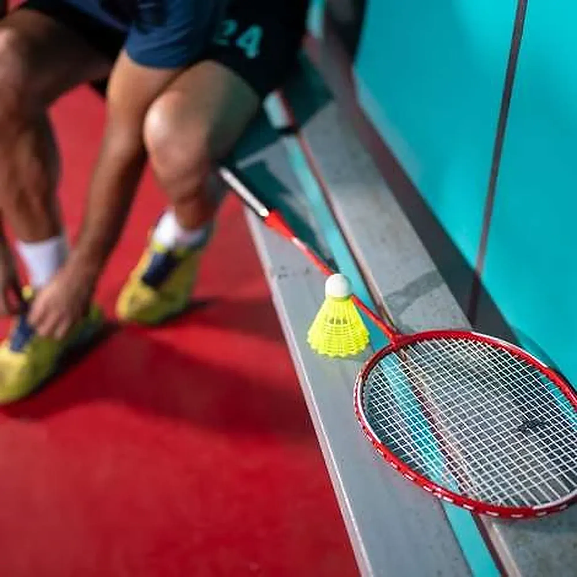 A player picks up a shuttle next to a racket on the court floor