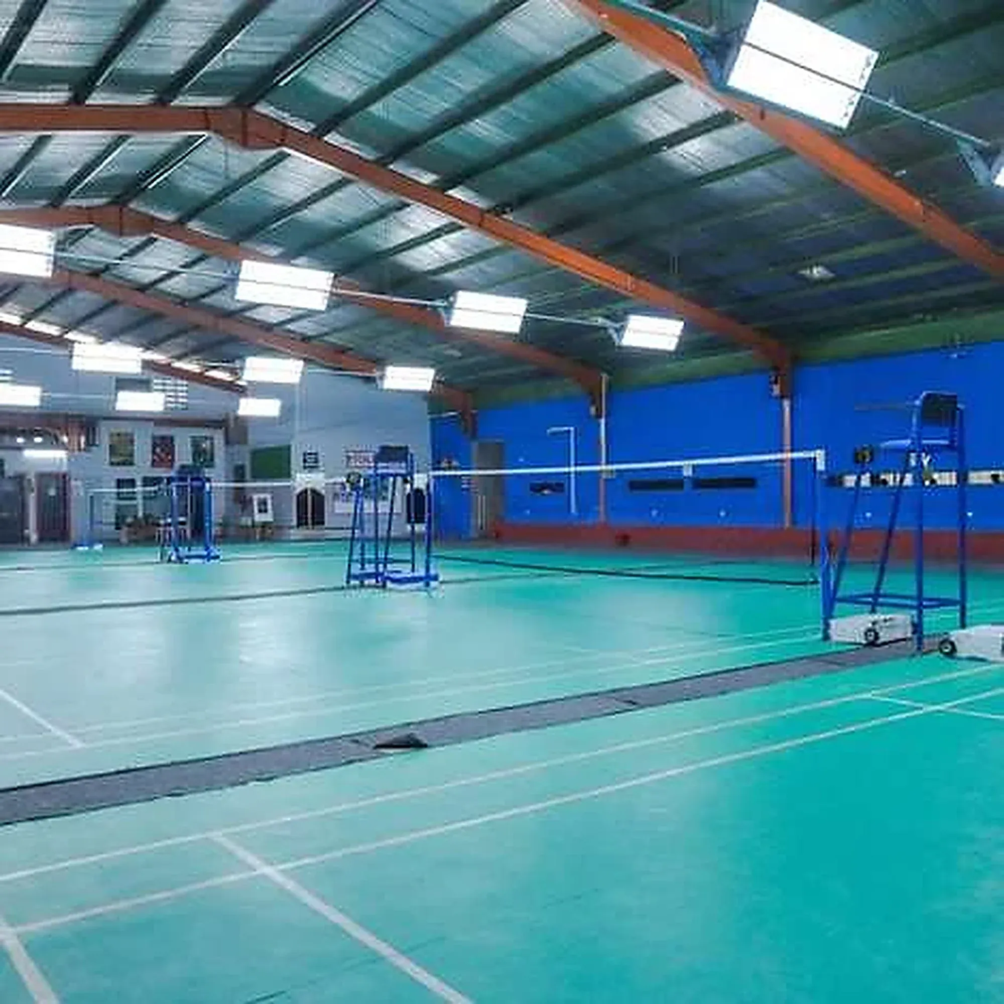 An empty badminton hall with green courts under bright lights